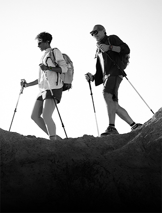 Two people wearing Apple Watch devices and hiking on a rocky trail with poles and gear